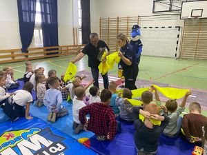 Policjanci i członek IPA rozdają dzieciom kamizelki odblaskowe.