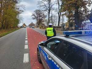 Policjant stoi przy radiowozie i obserwuje teren przy cmentarzu