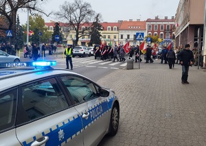 Policjant stoi przy drodze i obserwuje ruch zapewniając bezpieczeństwo uczestników marszu