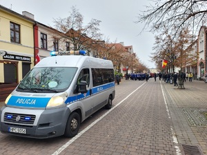 Policjant stoi przy drodze i obserwuje ruch zapewniając bezpieczeństwo uczestników marszu