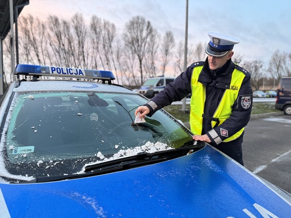 Policjant oczyszcza z lodu przednią szybę radiowozu