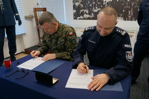Policjant oraz żołnierz podpisują porozumienie i pozują z dokumentami do zdjęcia