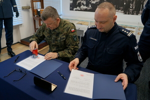 Policjant oraz żołnierz podpisują porozumienie i pozują z dokumentami do zdjęcia