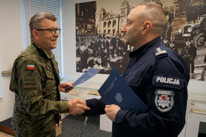 Policjant oraz żołnierz podpisują porozumienie i pozują z dokumentami do zdjęcia