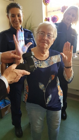 Seniorka ma podniesione ręce, a w tle stoją policjantki