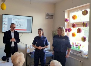 Dwie policjantki i emerytowany policjant stoją przed Seniorami