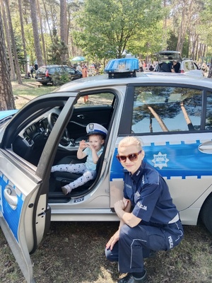 policjantka pozuje do zdjęcia przy radiowozie, w którym siedzi chłopiec