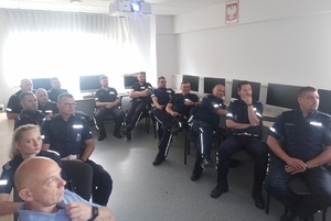 policjanci siedzą na krzesłach w sali i słuchają wykładu biegłego