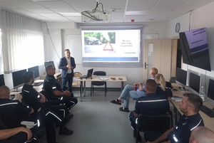 policjanci siedzą na krzesłach w sali i słuchają wykładu biegłego