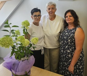 wizerunek trzech kobiet, na pierwszym planie na biurku stoi bukiet z hortensjami z napisem Hurra! Emerytura! Plik jpg.