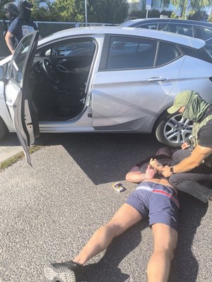 policjanci zakładają kajdanki mężczyźnie, który leży na ziemi obok samochodu