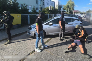 policjanci zakładają kajdanki mężczyźnie, który leży na ziemi obok samochodu