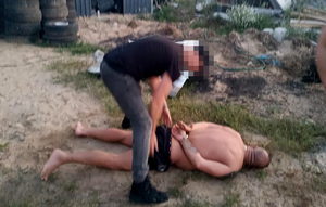 policjant pochyla się nad zatrzymanym skutym kajdankami leżącym na ziemi i wyciąga ręce na wysokości spodenek