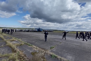 policjanci ćwiczą na płycie lotniska. Funkcjonariusze ustawieni są w szeregu. Pomiędzy nimi jedzie policyjny pojazd z wodą