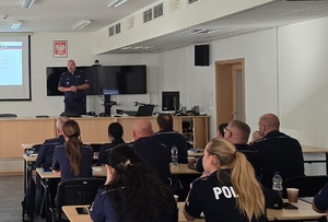 policjant przemawia do funkcjonariuszy siedzących w ławkach