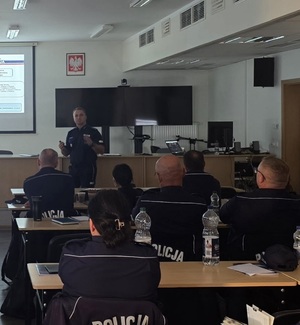 policjant przemawia do funkcjonariuszy siedzących w ławkach