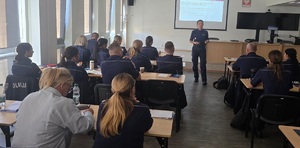 policjant przemawia do funkcjonariuszy siedzących w ławkach