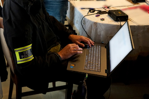 policjanci przeszukują pomieszczenia w domu podejrzanego i na komputerze sprawdzają zawartość nośników cyfrowych