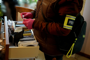 policjanci przeszukują pomieszczenia w domu podejrzanego i na komputerze sprawdzają zawartość nośników cyfrowych