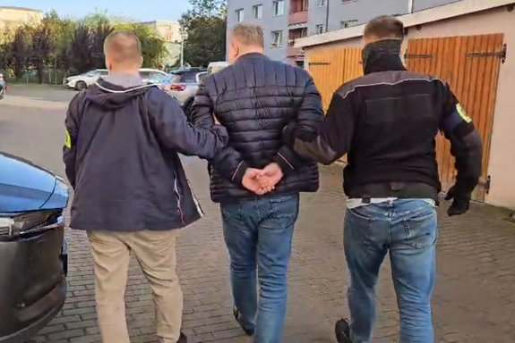 policjanci prowadzą mężczyznę skutego kajdankami