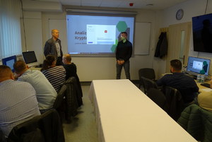 nieumundurowani policjanci siedzą przed komputerami i słuchają prowadzącego szkolenie