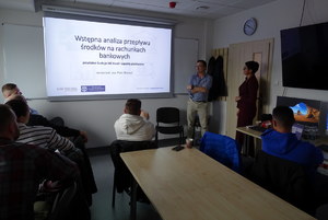 nieumundurowani policjanci siedzą przed komputerami i słuchają prowadzącego szkolenie