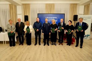 Osiem osób stoi w jednym rzędzie z zielonymi teczkami w dłoniach, gotowych do odebrania podziękowań. Za nimi widać ekran z informacją o dziesiątej edycji akcji.