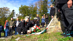 Dwie harcerki w mundurach składają kwiaty i znicz u stóp kamiennego pomnika, a wokół nich stoi grupa uczestników z Polski i Węgier. To moment symbolicznego upamiętnienia poległych żołnierzy.