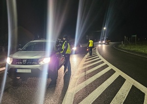 Policjantka kontroluje trzeźwość kierowcy a w tle drugi policjant podchodzi do innego kierującego