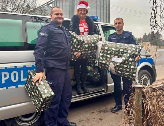 Dwaj policjanci i pani stoją z paczkami na tle radiowozu