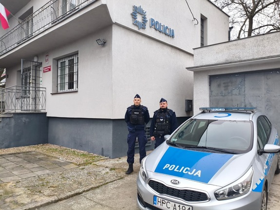 Policjanci przy radiowozie oraz miejsce pożaru domu.