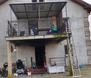 Policjanci przy radiowozie oraz miejsce pożaru domu.