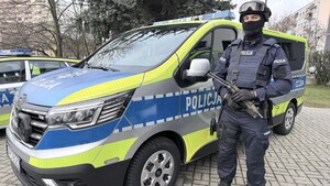 Umundurowany i uzbrojony policjant Grupy szybkiego reagowania przy oznakowanym radiowozie Renault Traffic