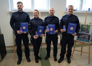 czterech policjantów trzyma otrzymane statuetki oraz teczkę z gratulacjami