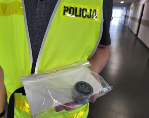 Policjant trzyma woreczek z pudełeczkiem, który ma symbol marihuany