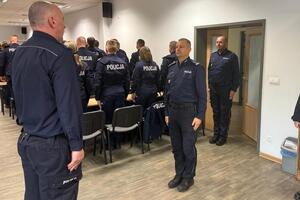 policjanci siedzą w ławkach i słuchają wypowiedzi stojącego przed nimi Komendanta