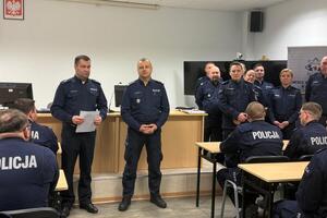 policjanci siedzą w ławkach i słuchają wypowiedzi stojącego przed nimi Komendanta