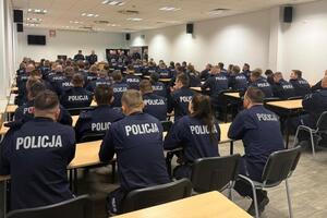 policjanci siedzą w ławkach i słuchają wypowiedzi stojącego przed nimi Komendanta