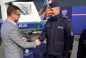 Wojewoda gratuluje i wręcza torebkę policjantowi