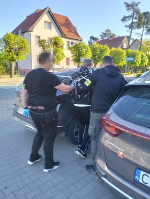 Policjanci konwojują zatrzymanego.