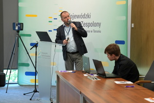 prelegent prowadzi szkolenie i mówi do zaproszonych gości siedzących w sali na krzesłach