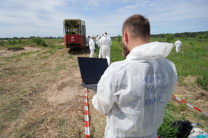funkcjonariusze ubrani w białe kombinezony przeprowadzają oględziny na miejscu zdarzenia