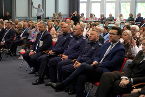 Inauguracja programu „Świadomy Senior – Bezpieczny Senior” zaproszeni goście i seniorzy siedzą na krzesłach w auli