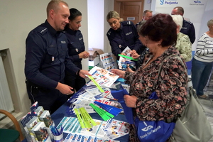 przy stoisku policyjnym stoją seniorzy, policjanci rozdają im przegotowane dla nich gadżety