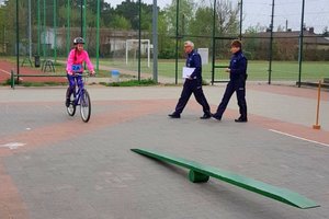 policjanci przyglądają się jak dziewczynka przejedzie na rowerze przeszkodę