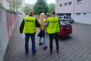 Dwaj policjanci prowadzą skutą w kajdanki kobietę do policyjnego pojazdu