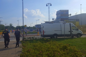 dwaj policjanci patrolują teren przy stadionie. Obok stoi samochód Mobilne Centrum Monitoringu