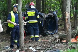 policjant i strażacy stoją przy rozbitym aucie