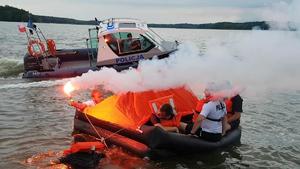 Ćwiczenia na Zalewie Koronowskim. Policyjna łódź motorowa podpływa do osób na tratwie. Osoby te odpaliły race świetlne.