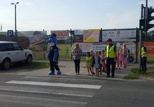 Dzieci pod okiem policjantów ćwiczą przechodzenie przez przejście dla pieszych.